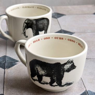 Two mugs with bear and elephant illustrations on a tiled surface