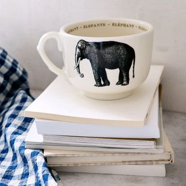 White mug with black elephant design on a stack of books with a blue checkered towel.