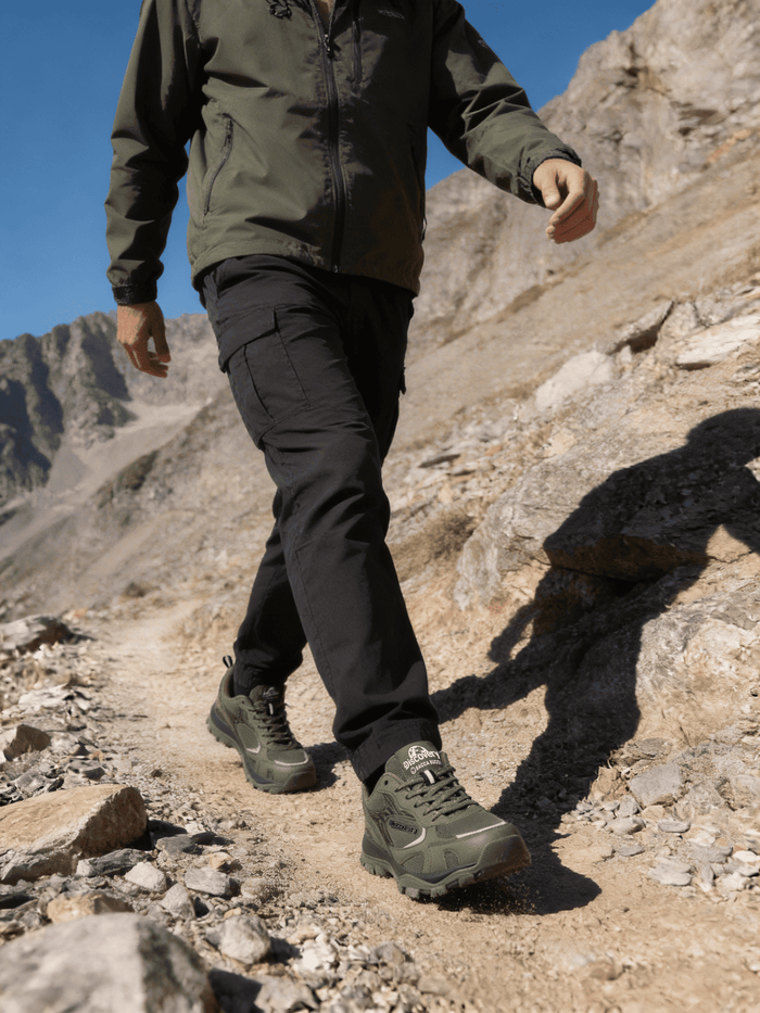 Person hiking on a rocky mountain trail wearing green jacket and black pants.