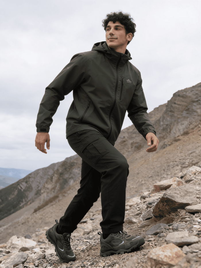 Man in green hiking jacket and pants standing on a rocky mountain peak