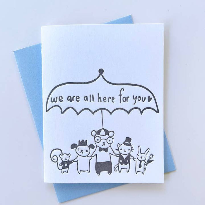 Card with illustration of animals under an umbrella and text 'we are all here for you' on a blue background