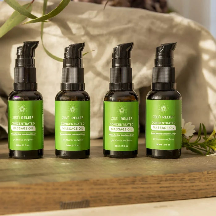 Zea Relief Concentrated Massage Oil - 4 lined up in a row on a wooden board and linen in the background.
