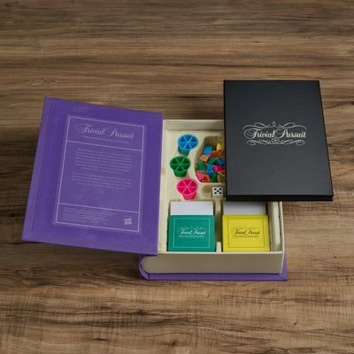 Trivial Pursuit game box with colorful question cards on a wooden surface