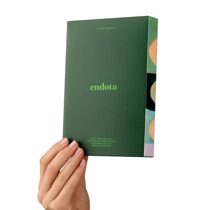A hand holding a dark green Endota mask set box against a solid white background. The box features the brand name 'endota' in light green text and displays a colourful side panel with abstract circular patterns.
